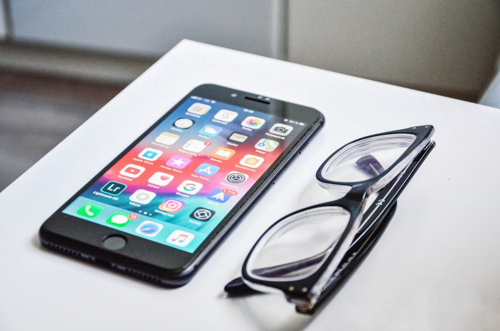 phone on with apps next to glasses on desk